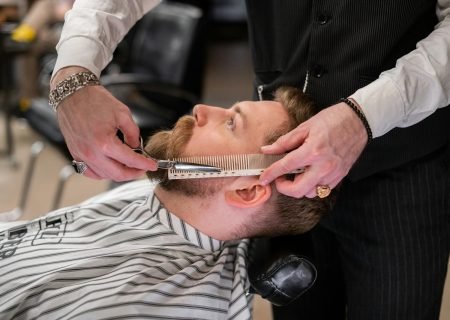 A skilled barber meticulously trims a client's beard using comb and scissors in a modern barbershop.